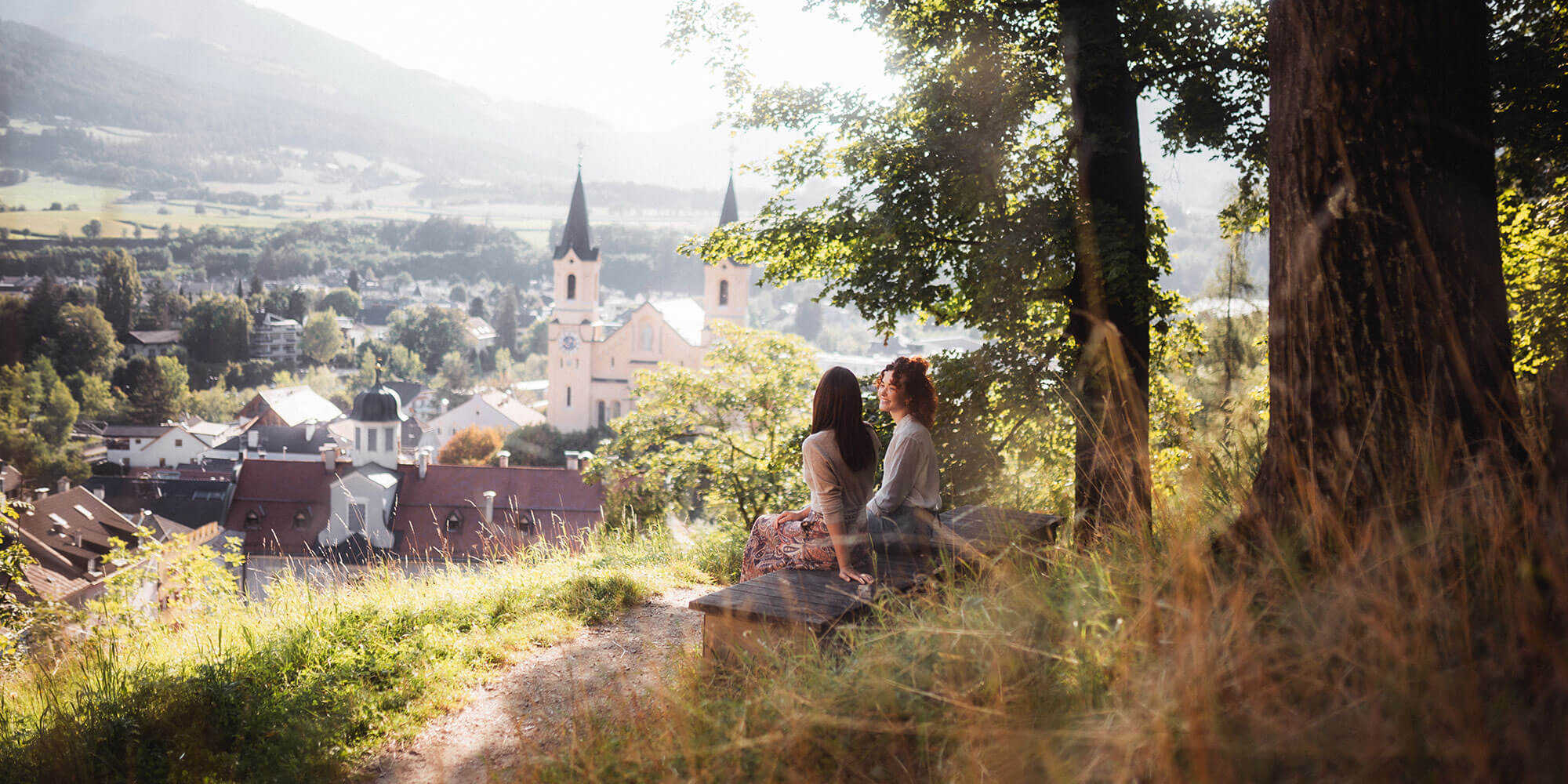 Brunecker Pfarrkirche und 2 Frauen auf einer Bank